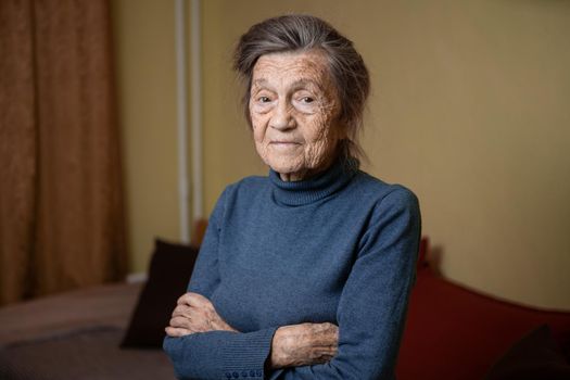 Older cute woman of ninety years old Caucasian with gray hair and wrinkled face looks at camera, cute kind look and smiles.Mature grandmother retired long-liver, theme emotion and mood of old people.