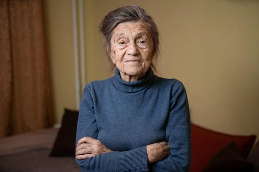 Elderly Caucasian senior grandmother ninety years old looks attentively and smiles, feels happy, large portrait, face with deep wrinkles, gray hair. Theme pensioners, old people and long-lived woman.