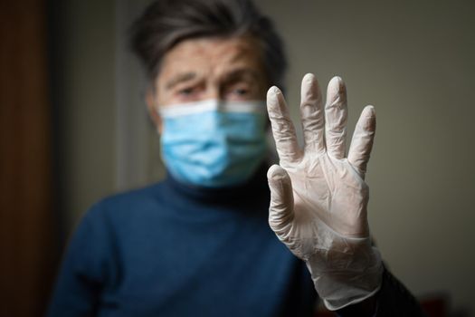 Importance wearing gloves and masks to protect of coronavirus, especially elderly and seniors. Focus on latex gloves on background old woman in medical mask. Sign indicates protection against covid 19