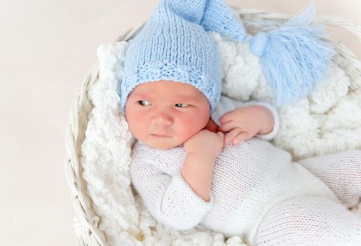 Cute newborn in knitted suit and hat lying in white basket