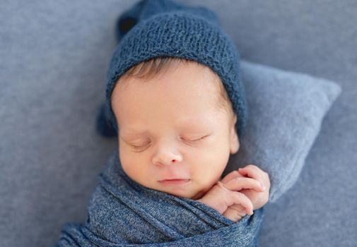 Cute asleep newborn wrapped in blanket wearing blue knitted hat