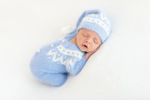 Lovely newborn in blue knitted suit sleeping with open mouth