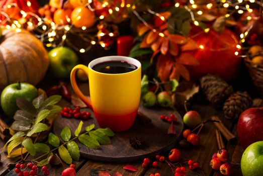 red and yellow mug with mulled wine. Fruits and spices are all around on a wooden table. lights of garlands are burning behind