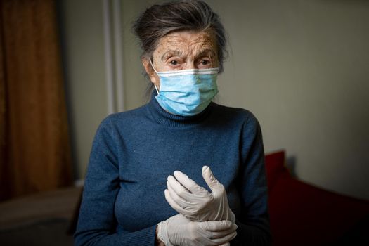 Old Caucasian woman dressed in personal protective equipment, mask and gloves, encourages to stay at home during an epidemic for safety. Health care and elderly care theme.