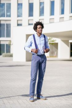 Black businessman with afro hairstyle wearing shirt and suspenders standing near an office building.