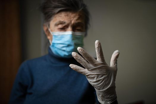 Theme equipment to protect against infection and bacteria during the coronavirus pandemic. The importance of wearing medical gloves for old people, senior woman shows her example to stay at home.