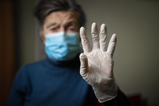 Theme equipment to protect against infection and bacteria during the coronavirus pandemic. The importance of wearing medical gloves for old people, senior woman shows her example to stay at home.