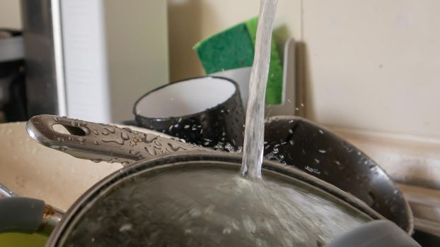 The kitchen utensils in the wash basin need to be washed. A pile of dirty dishes in the kitchen sink with running water. Kitchen utensils need washing. Homework concept
