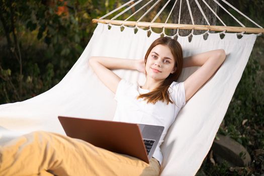 woman outdoors with laptop lies in hammock leisure technology. High quality photo