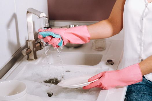 housewife girl in pink gloves washes dishes by hand in the sink with detergent. The girl cleans the house and washes dishes in gloves at home