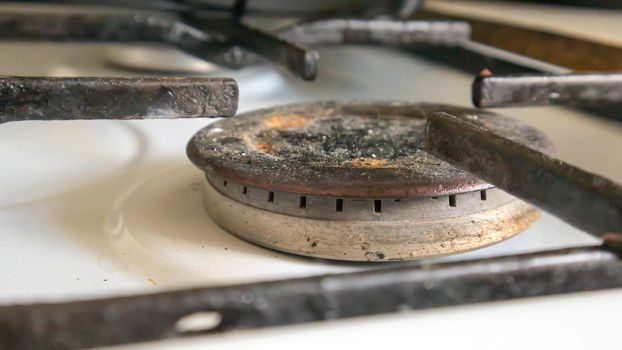 Dirty gas stove in the kitchen for cooking with vegetable oil stains and burnt food debris on the surface, close-up. Selective focus. Grease-covered gas hob in the kitchen