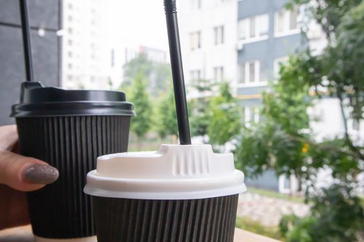 Two black paper coffee cups with lids outdoors in summer in sunny weather on a wooden table of a cafe, coffee shop or restaurant