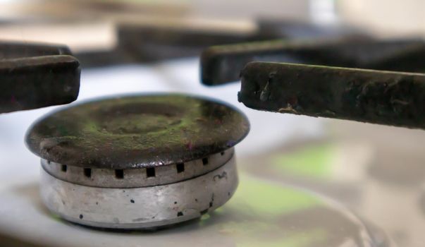 Dirty gas stove in the kitchen for cooking with vegetable oil stains and burnt food debris on the surface, close-up. Selective focus. Grease-covered gas hob in the kitchen