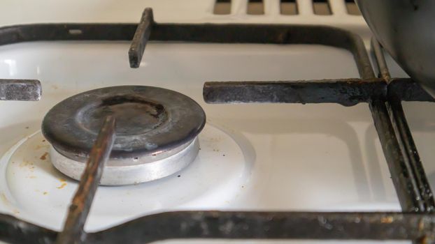 Dirty gas stove in the kitchen for cooking with vegetable oil stains and burnt food debris on the surface, close-up. Selective focus. Grease-covered gas hob in the kitchen