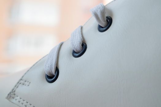 White leather sneakers lace-up shoes. White laces are tied close-up. Blurred background. Sports concept. Metal rivet for shoes as a detail or an element. Fashionable and stylish footwear