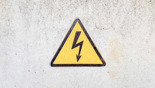 Danger sign of high voltage electricity. Yellow triangular sign with a lightning in the center. This warning is written on an old metal surface painted with gray paint