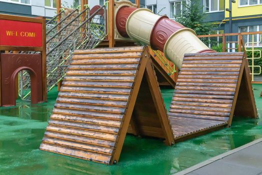 A courtyard of high-rise buildings with a modern and large playground made of wood and plastic on a rainy summer day without people. Empty outdoor playground. A place for children's games and sports