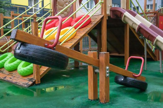 A courtyard of high-rise buildings with a modern and large playground made of wood and plastic on a rainy summer day without people. Empty outdoor playground. A place for children's games and sports