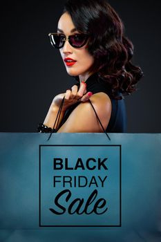 Beautiful young woman make shopping in black friday holiday. Girl with black bag on dark background.