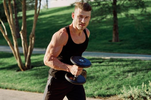 athletic man in black t-shirt with dumbbells in the park training. High quality photo