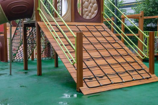 A courtyard of high-rise buildings with a modern and large playground made of wood and plastic on a rainy summer day without people. Empty outdoor playground. A place for children's games and sports