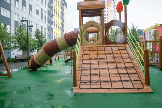 The courtyard of a high-rise building with a modern large playground made of wood and plastic on a rainy summer day without people. Ukraine, Kiev - August 19, 2021