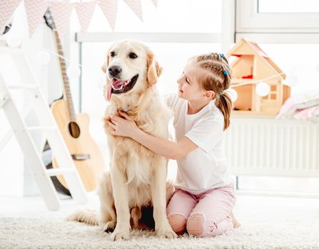 Happy little girl cuddling beautiful dog in children's room