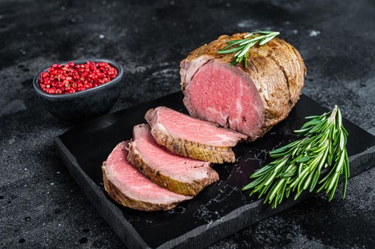 Roast beef fillet Tenderloin meat on a marble board. Black background. Top view.