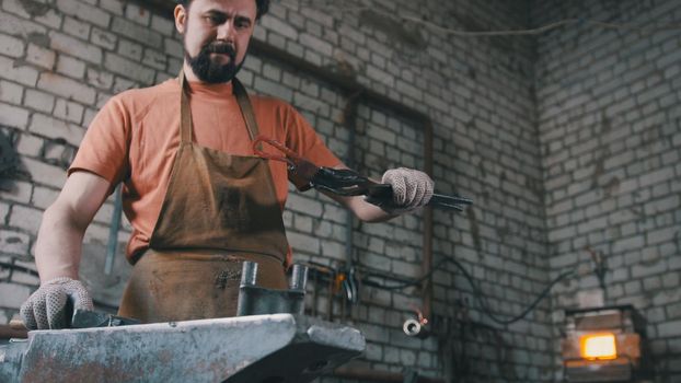 Muscular blacksmith in forge hammering steel products, small business