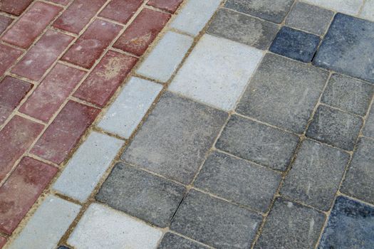 Concrete or paved newly laid gray and red paving slabs or stones for floors or walkways. Concrete paving slabs in the backyard or road paving. Garden brick path in the courtyard on a sandy foundation