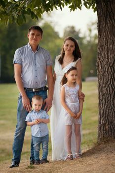 Cheerful family in a park at summer evening - father, mammy, daughter and little boy, portrait