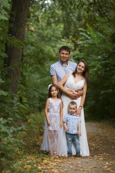 Healthy family posing in the green park - father, mammy, daughter and little boy, vertical shot