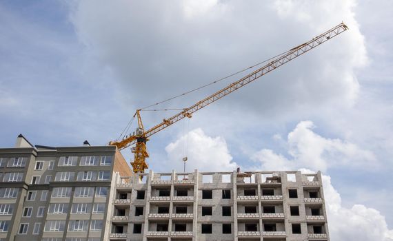 Construction crane on an unfinished residential building against the sun and blue sky. Housing construction, apartment building in the city. Construction site of residential buildings