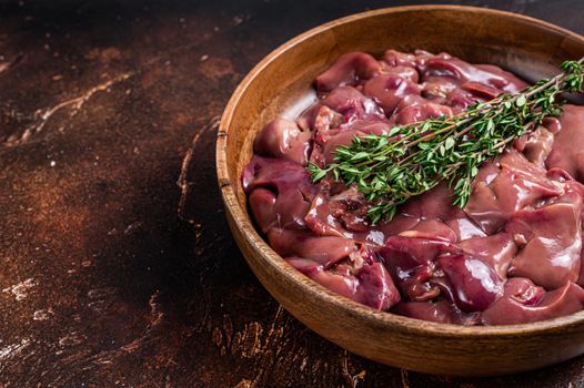 Raw chicken liver offals in a wooden plate. Dark background. Top view. Copy space.