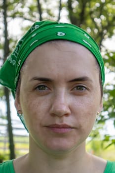 Portrait, close-up. Beautiful young woman without makeup in a green T-shirt and a green headdress from the sun on a sunny summer day outdoors. Sunlight. Vertical photography