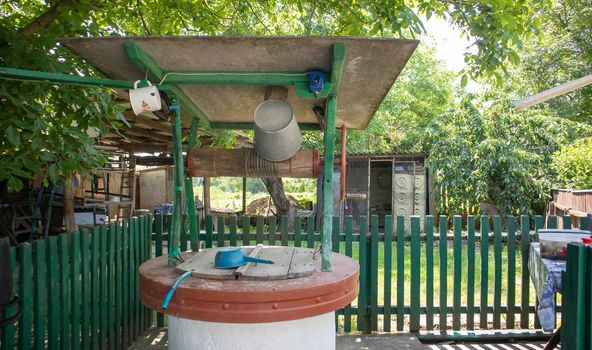 An old water well with a bucket in the garden, a metal handle for lifting water from the ground. Village well under the roof with a rope. Retro well in the countryside