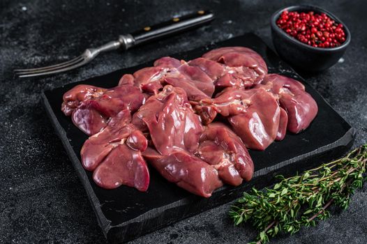 Raw chicken liver meat on marble board with thyme. Black background. Top view.