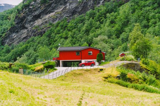 July 20, 2019. Norway. Flam. Red wooden house and cars in Norwegian Flam town. Country house and car on the yard. Cottages in mountains.