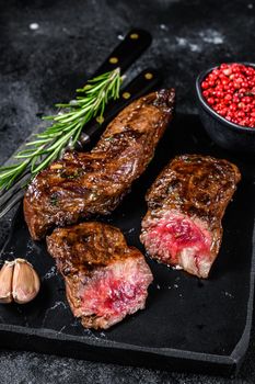 Grilled brisket steaks in bbq sauce on a marble board. Black background. Top view.