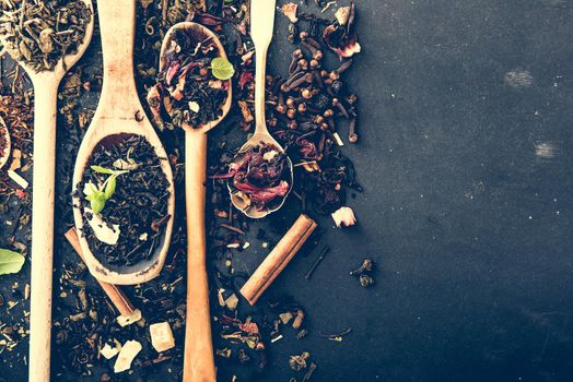 Virious kinds of tea in wooden spoons on black table