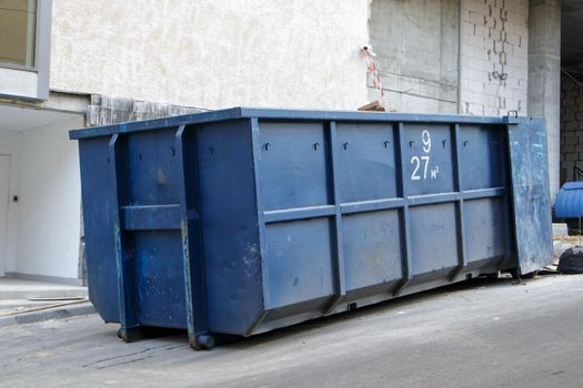 Metal durable blue industrial trash bin for outdoor trash at construction site. Large waste basket for household or industrial waste. A pile of waste