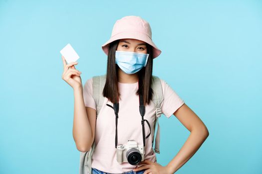 Happy korean tourist, girl on vacation standing with credit card and camera, paying for souvenirs, travelling abroad, standing over blue background.