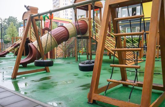 The courtyard of a high-rise building with a modern large playground made of wood and plastic on a rainy summer day without people. Ukraine, Kiev - August 19, 2021