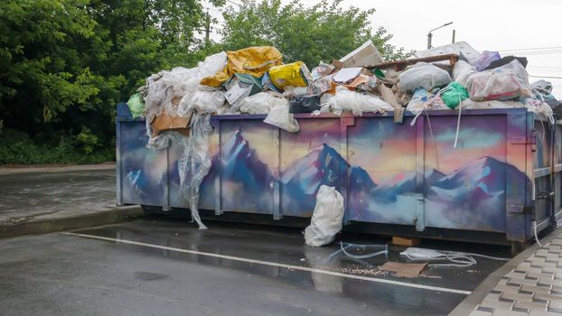 Metal durable blue industrial trash bin for outdoor trash at construction site. Large waste basket for household or industrial waste. A pile of waste. Ukraine, Kiev - August 09, 2021