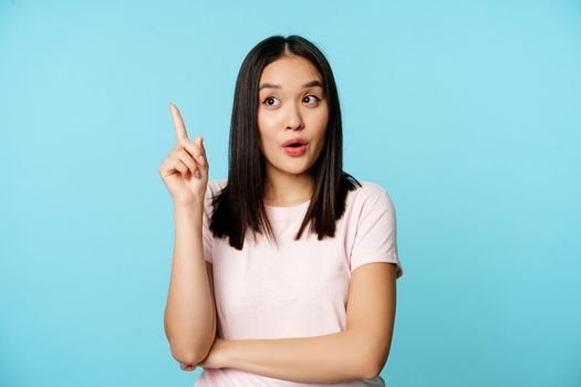 Eureka. Young asian woman found solution. Korean girl raising finger up and pitching an idea, standing thoughtful over blue background.