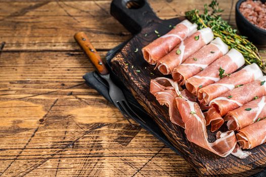 Prosciutto crudo Dry cured parma ham on a wooden cutting board with thyme. wooden background. Top View. Copy space.