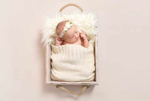 Adorable child wearing hairband laying in a baby basket with her eyes opened widely, closeup