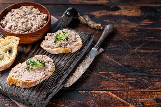 Toasts with Duck pate Rillettes de Canard on wooden board. Dark wooden background. Top View. Copy space.