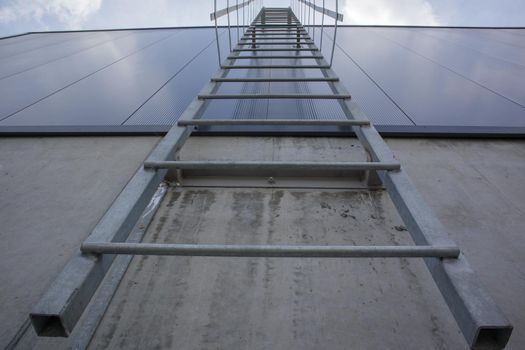 Fire escape on the industrial building above, bottom view. Stainless steel handrails, roof ladder. Detail view of stairs with safety cage. Building construction concept