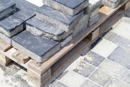 Concrete or paved gray paving slabs or floor or walkway stones stacked on a pallet. Concrete paving slabs in the backyard or road paving. Garden brick path in the courtyard on a sandy foundation